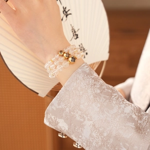 Close-up of triple-strand white crystal beaded bracelet with golden heart charms