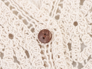 Close-up of geometric crochet pattern and natural coconut button on beige cardigan