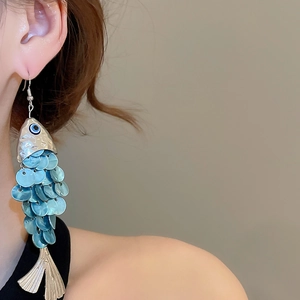 Detail of fish-shaped shell tassel earring with blue sequins worn by a model