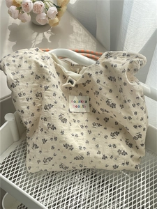 Close-up of floral canvas tote bag with woven handles and brand label in a mesh cart