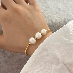 Detail of twisted gold bracelet with three white freshwater pearls and textured finish