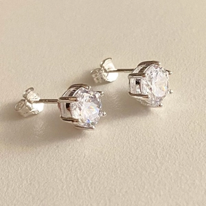 Close-up of classic six-prong stud earrings with clear zircon stones on a neutral surface