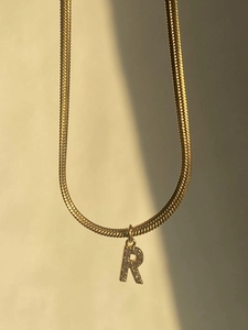 Detailed close-up of golden flat snake bone necklace with sparkling diamond-set R pendant