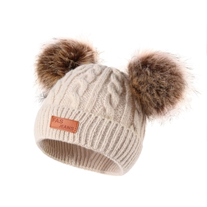 Detail of cable knit winter hat with double faux fur pom-poms and leather patch