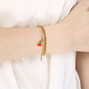 Detail of double-layer gold chain bracelet featuring a charming red cherry pendant on wrist