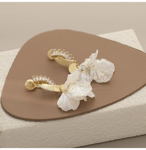 Dettaglio di orecchini dorati con pendenti a petalo bianco e cristalli scintillanti