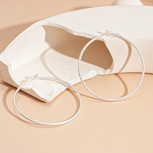 Close-up of large silver hoop earrings with a textured frosted finish on a neutral base