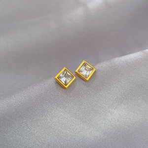 Macro shot of square zircon stud earrings with gold frames on a soft satin background