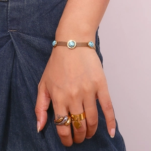 Detail of gold mesh bracelet with turquoise stones and heart pendant ring on model