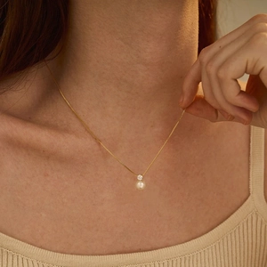 Detail of elegant gold-tone chain necklace with pearl and zircon pendant on model