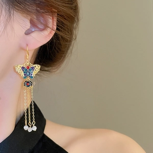 Detail of gold butterfly tassel earrings with colorful enamel and white bead accents