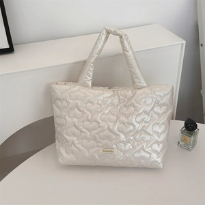 Detail of silver heart quilted tote bag with smooth metallic finish and woven brand label