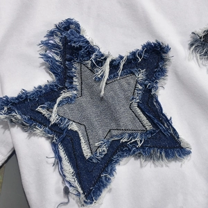 Close-up of blue denim star patch with frayed edges on a white cotton t-shirt