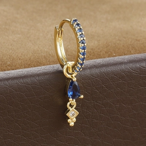 Macro detail of gold-plated hoop earring with teardrop blue zircon on brown leather