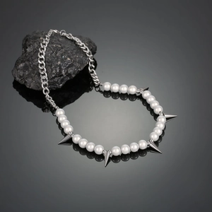 Detailed view of hip hop style necklace with pearls and metallic spikes on dark rock