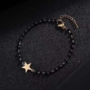 Detail showing golden star pendant on a black beaded bracelet with gold chain