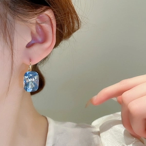Macro view of gold hoop earrings with large rectangular blue faceted crystal gemstone