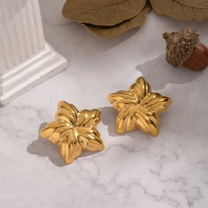Détail de boucles d'oreilles étoiles en or 18K sur marbre avec décor naturel