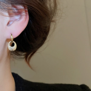 Close-up of golden oval hoop earrings with woven texture and vintage hammered finish