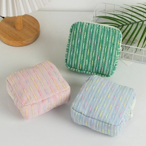 Three colorful striped cosmetic bags with white zippers in a cozy home setting