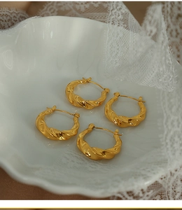 Détail macro de boucles d'oreilles torsadées dorées sur une assiette en céramique