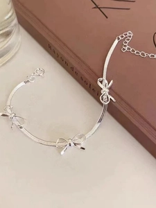 Detail of silver snake chain bracelet featuring three polished bow charms and a lobster clasp