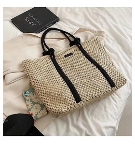 Detail of hollow woven texture and black rope handles on a beige straw tote bag