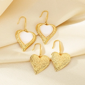 Detailed view of gold heart earrings with white cat eye stone on silk fabric background