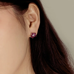 Detail view of a floral silver stud earring with rose red crystals on female model