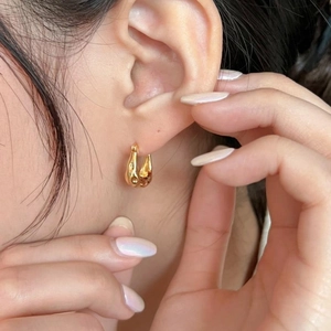 Macro detail of irregular golden waterdrop hoop earrings worn on a model's ear