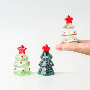 Macro view of three miniature glass Christmas trees with tiny red stars on white background