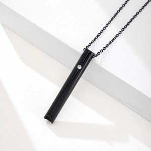 Black stainless steel meditation whistle necklace with crystal inlay on a white background