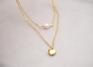 Macro detail of double-layered gold heart necklace with white freshwater pearl accent