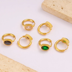 Flat lay of gold oval zircon earrings in white, black and green colors on stone