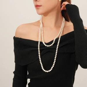 Detail of elegant multi-layered long pearl necklace worn on black sweater for women