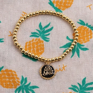 Detailaufnahme eines goldenen Perlenarmbands mit schwarzem Be Free Emaille-Anhänger