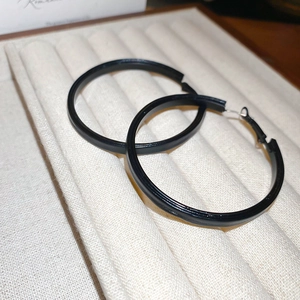 Macro view of minimalist matte black geometric hoop earrings on a beige velvet jewelry tray