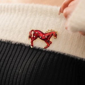 Detailed view of a vintage horse brooch with red enamel and crystals on a white sweater