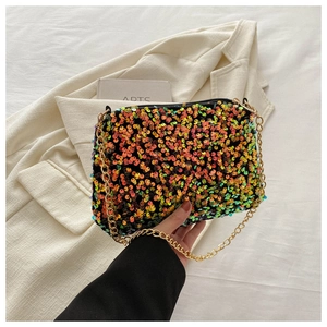 Close-up of small sequin crossbody bag with gold chain strap on a white blazer