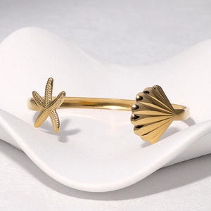 Golden starfish and shell stainless steel open cuff bracelet on white textured display
