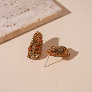 Detail of vintage gold earrings with orange rhinestones and geometric teardrop design