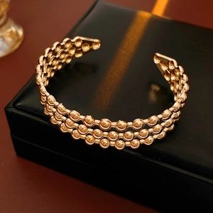 Dettaglio macro di un bracciale rigido a tre strati con sfere in oro rosa su box nero
