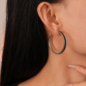 Close-up of a silver C-shaped hoop earring with black zircon pave on a female model