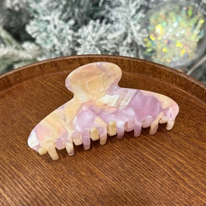 Close-up of a marbled purple and pink acetate hair claw clip on a wooden display tray