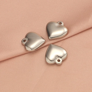 Polished solid stainless steel heart charms on pink fabric, detail of three silver pendants