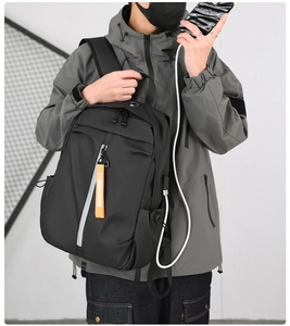 Detail of black travel backpack showing built-in USB charging port with orange ribbon