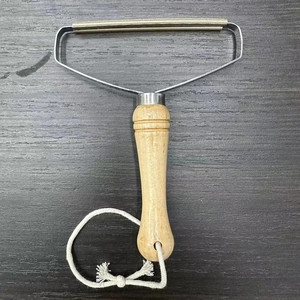 Detail of manual lint remover with wooden handle, metal frame, and hanging cotton rope