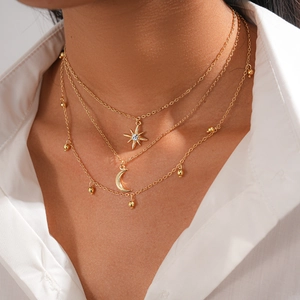 Detail of layered gold star and moon pendant necklace worn over a white shirt