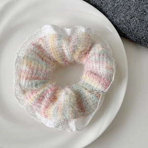 Close-up of a rainbow knit hair scrunchie with white lace trim and fluffy texture on a plate