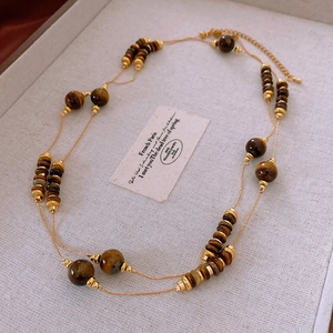 Detail of layered gold necklace with dark brown faux tiger eye beads on jewelry tray